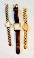 Three women's wristwatches displayed on cloth background: Esquire watch with gold-tone linked bracelet, Anne Klein with square face and leather strap, and a Seiko gold-tone linked watch.