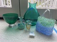 Five art glass pieces displayed on a light carpet including bowl, vases, and handbag-shaped item.