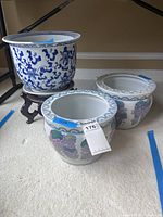 Three Asian jardiniere pots and one wooden stand on carpeted floor, showing size and relative positioning.