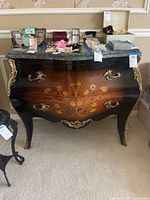Front view of bombe style dresser showing floral inlay, gold ornaments, and marble top with some scratches and scuffs.