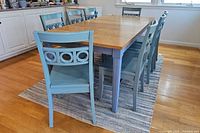 Set of eight blue wooden dining chairs around a table, showing overall appearance and condition including scratches.