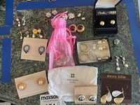 Full overview of assortment of costume jewelry earrings including pearl studs, rhinestone hoops, clip-ons, studs in branded pouches