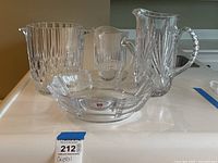 Four clear crystal items including three pitchers with vertical cuts and one square scalloped bowl, all with Orrefors Sweden labels.