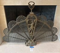 Front view of brass peacock-style folding fireplace fan screen in front of fireplace