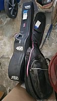 Black hard guitar case and black soft gig bag guitar case on concrete floor.