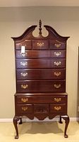 Front view of the high boy chest showing 11 drawers, decorative brass handles, and ornate top finial.