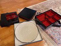 Photo showing two Japanese lacquer bento boxes with red compartments and a Lenox cream embossed platter on a box.