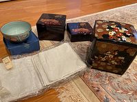 Overview of the full lot: three lacquer boxes, one ceramic bowl, and white cloth napkins.