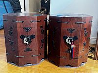 Two octagonal wooden cabinets with intricate black metal hardware on corners and sides, placed on a wooden floor.