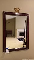 Frontal image of the wood framed mirror hanging on a beige wall with a visible fireplace and furniture reflected in the mirror.