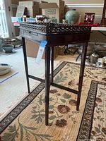 Side view showing the tall slender legs, lattice top edge, and pull-out candle rest under the drawer.