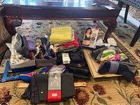 View of scarves, socks, slippers under a table on carpet, includes boxed bra and wrapped socks.