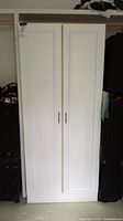 Front view of the closed white laminate storage cabinet with double doors and silver handles.
