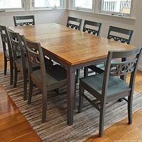 Side view of farmhouse dining table with natural wood top and dark painted legs around with multiple chairs.