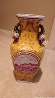 Front view of yellow ceramic vase showing scenic inset with a building and floral decoration.
