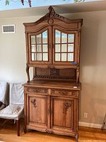 Full view of the two-piece oak china cabinet buffet showing carved crest, glass-panel doors, drawers and lower cabinet doors