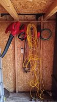View of yard tools including red blowers, hedge trimmers, and extension cords hung on wall