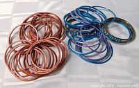 Photo showing a collection of copper-tone and blue-tone metal bracelets arranged on a white surface.
