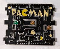 Front of the rectangular metal belt buckle showing Pac-Man video game theme with characters and maze design in black, yellow, green, orange, and beige.