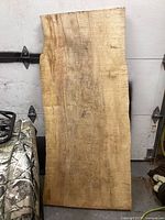 Front view of the hardwood live edge slab leaning against a door showing natural wood grain, live edges, and slight discoloration.