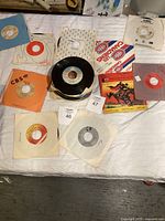Mixed lot of 45 RPM vinyl records laid out on a bed with various colored and branded sleeves visible including CBS and Capitol.