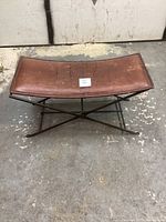 Top front view of antique leather seat on collapsible black steel legs showing worn leather surface and seat shape.