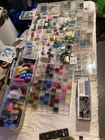 Full overview of beading supplies spread across a table, showing bead storage boxes, plastic bags, and spools of beading thread and wire