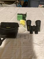 Black Bushnell binoculars alongside a soft carrying case, cleaning cloths, lens cover, and instruction manual all placed on a white surface.