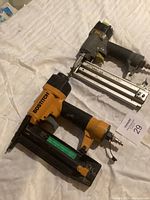 Two pneumatic brad nailers side by side on white fabric background.