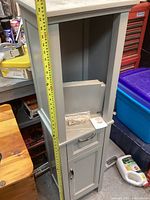 Gray wooden cabinet with measuring tape showing height of approximately 58 inches and drawer and door visible.