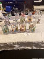 Overall view of 14 collectible character glasses arranged on a table showing variety of brands and animations.