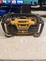 Front view of DeWalt yellow portable jobsite radio with black protective tubular frame, showing control panel and speakers.