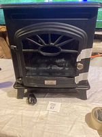 Front view of black electric stove heater with decorative vented glass door and metal knob.