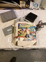 PlayStation One console, Nintendo Wii game and box, Wii manual laid out on white cloth - showing gaming consoles and game materials