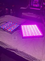 Two LED grow light panels lit and showing colored lights on a cloth surface.