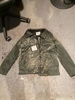 Front view of green satin-like jacket showing zip and snap button closure with two front pockets and collar detail.