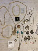 Flat lay of entire jewelry lot showing various necklaces, earrings, rings, and pendants on beige fabric background.
