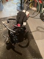 Photo showing black three-wheel push bike with padded, high-back seat and safety harness, along with front handlebar and pedals.