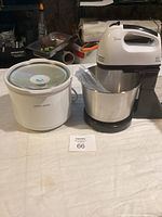 Black & Decker slow cooker with glass lid next to electric hand mixer and stainless steel bowl on table.