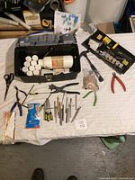Overview of tools spread on white cloth including plastic boxes with adhesive bottles, pliers, screwdrivers and metal tools