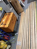 Eight oak boards laid out on a concrete garage floor, some labels attached. Background shows a wooden chest and some garage tools.