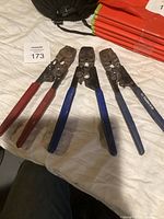 Three PEX crimping tools on a white surface, two with blue Watermark-branded handles and one with red handles, showing signs of wear.