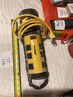 ProPower yellow power strip with six outlets, power switch, and yellow cord coiled around it on a white surface next to a measuring tape highlighting length.