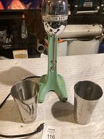 Front view of vintage Hamilton Beach drink mixer with two stainless steel cups on a white table.