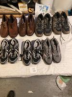 Overview of seven pairs of men's size 9 shoes laid out on a white surface including brown casual shoes, hiking shoes, and athletic sneakers.