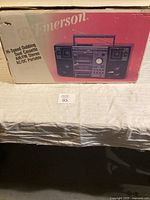 Box featuring Emerson branding and product image showing the boombox with dual cassette decks, AM/FM radio, and speakers.