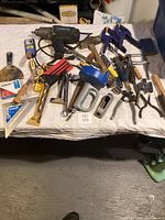 Full view of lot including power drill, hammers, clamps, putty knives, screwdrivers, and other hand tools spread across a table.