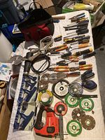 Full view of the lot laid out on a white cloth showing tool bag, pliers, screwdrivers, power tools, and cutting discs.