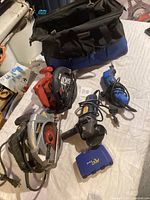 Lot contents including multiple power tools and tool bag on white surface