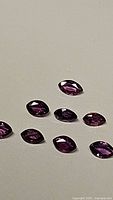 Close-up photo showing eight marquis cut deep purple sapphires arranged on a plain surface, highlighting color and clarity.